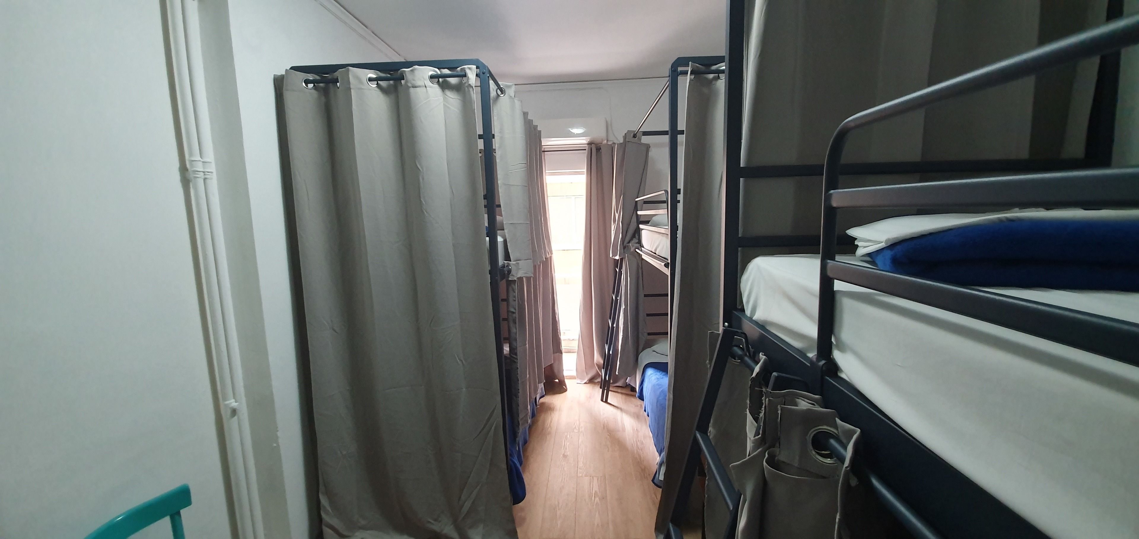 A narrow corridor with bunk beds on one side and a curtain-covered window on the other.