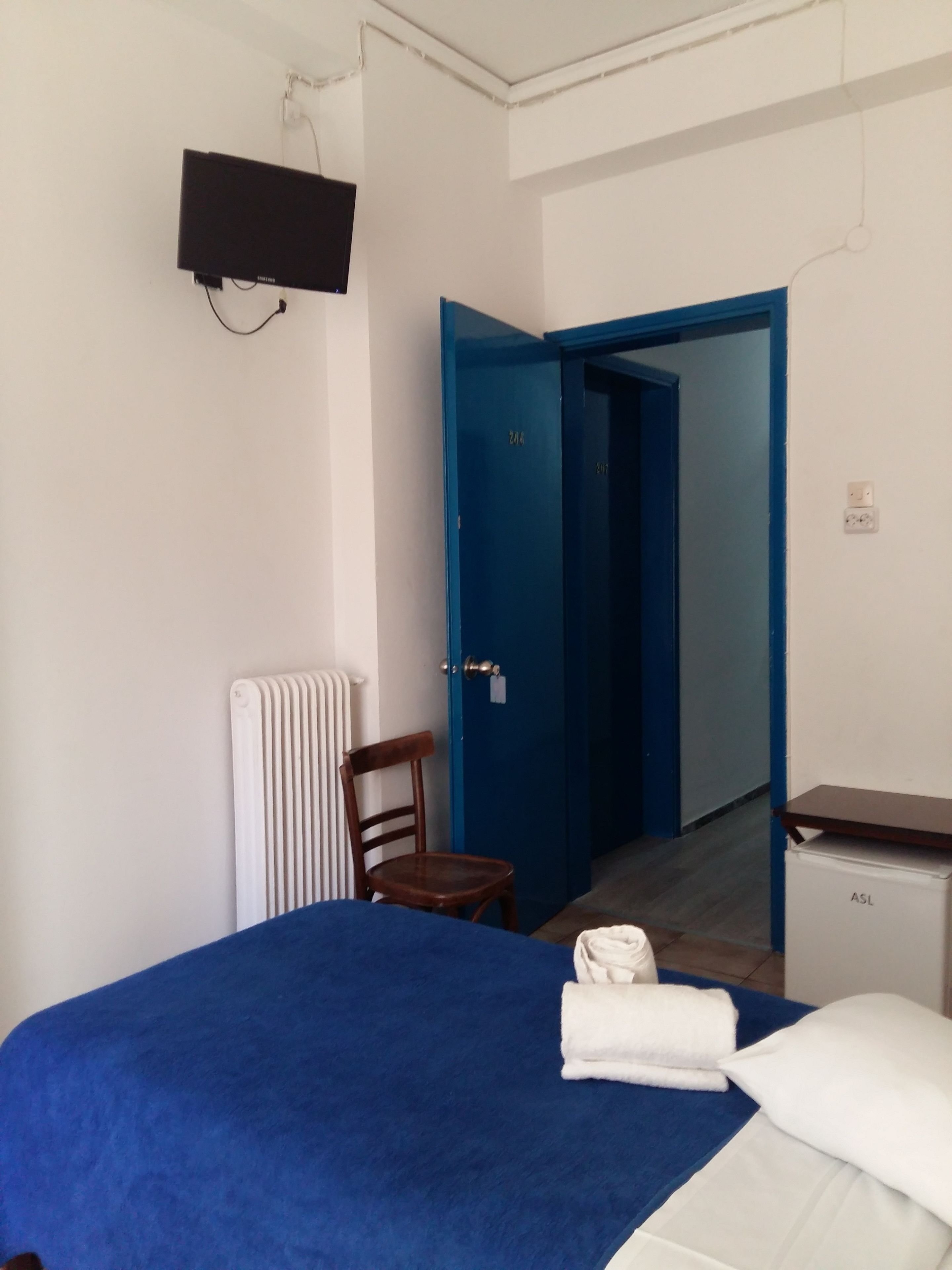 A bedroom with a bed, a chair, a radiator, a TV mounted on the wall, and a door leading to another room.