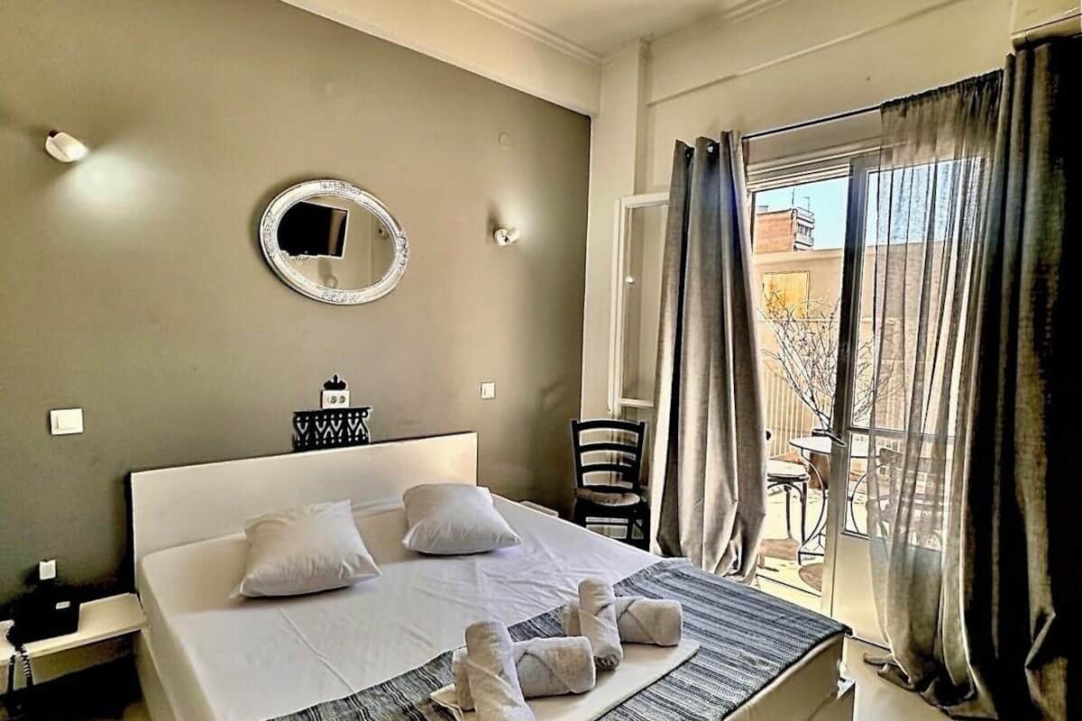 A hotel room with a large bed, a bedside table, a chair, and a view of the outdoors through a window with curtains.