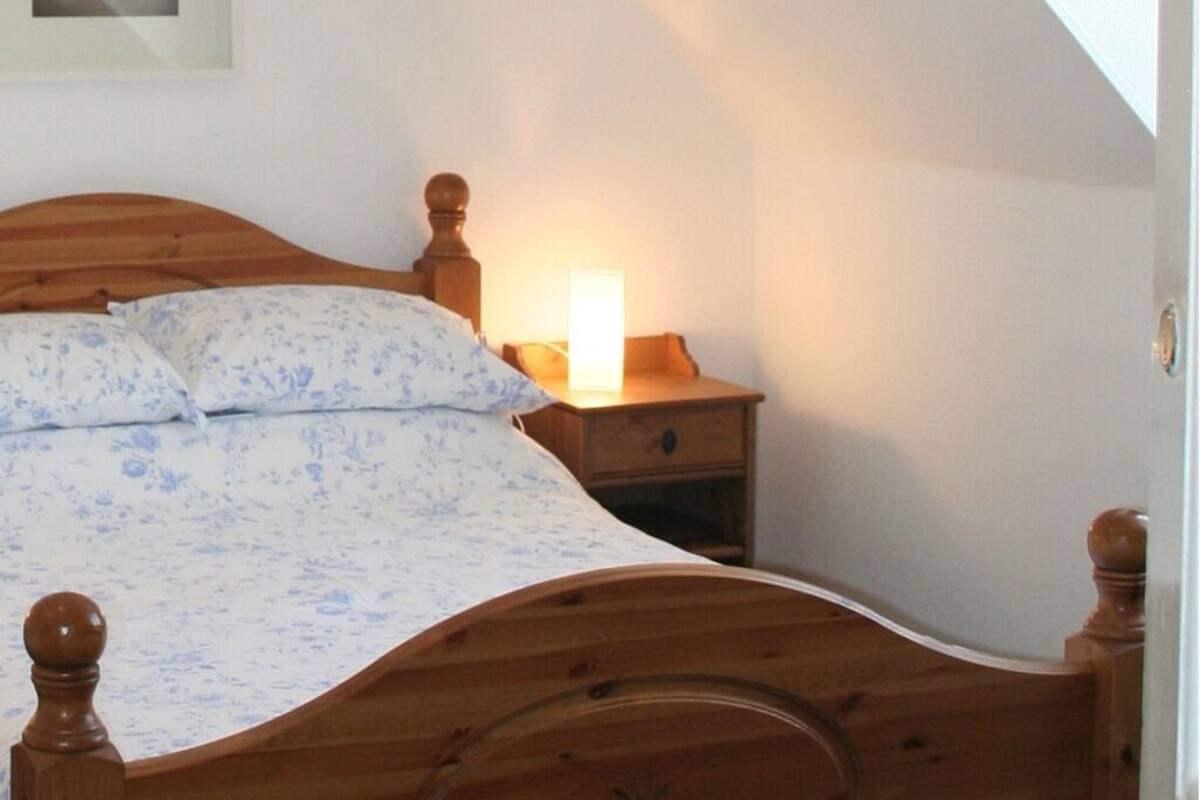 A bedroom with a wooden bed, a bedside table with a lamp, and a nightstand.