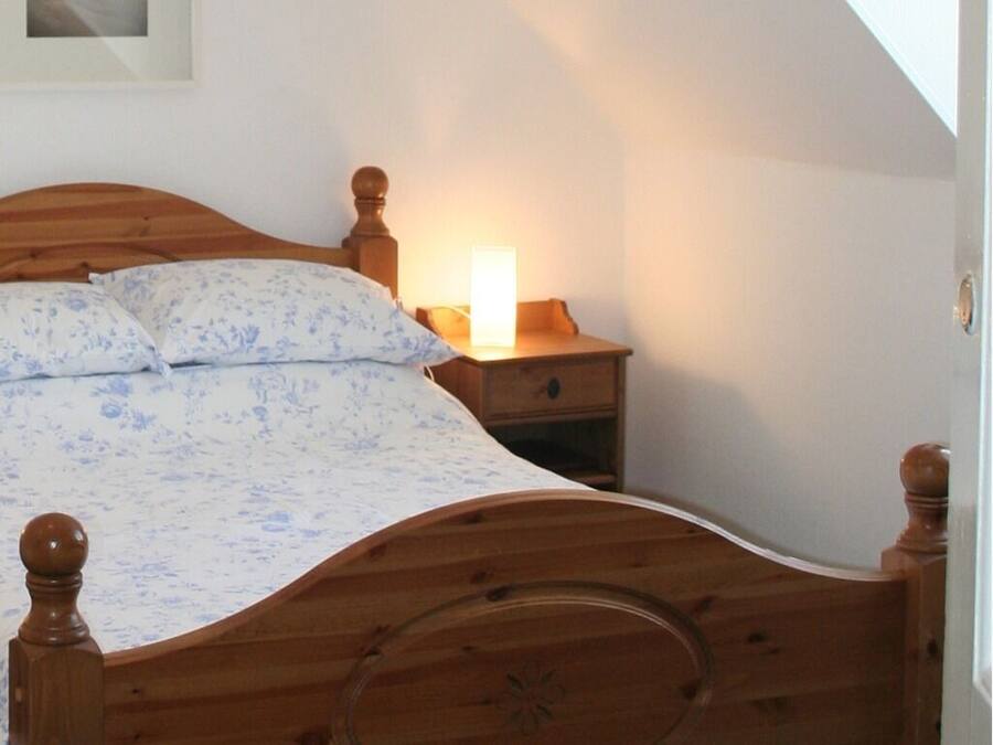 A bedroom with a wooden bed, a bedside table with a lamp, and a nightstand.