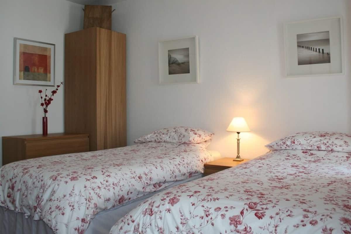 A bedroom with two beds, a nightstand, a lamp, and framed pictures on the wall.
