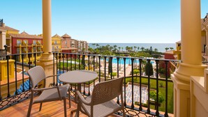 Ein Balkon mit zwei Stühlen und einem Tisch, Blick auf einen Pool und das Meer.