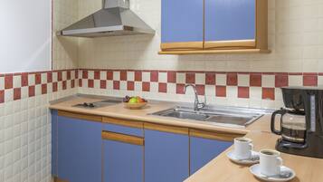 A kitchen with a sink, two cups of coffee, a fruit bowl, and a coffee maker.