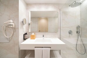 A modern bathroom with a large mirror, a white sink, a handheld showerhead, and a hairdryer.