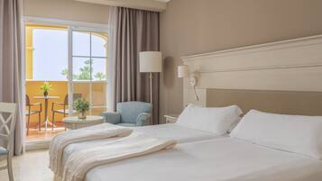 Habitación de hotel con una cama grande, una mesa redonda pequeña con sillas, un sillón azul y vistas al exterior a través de un ventanal amplio.