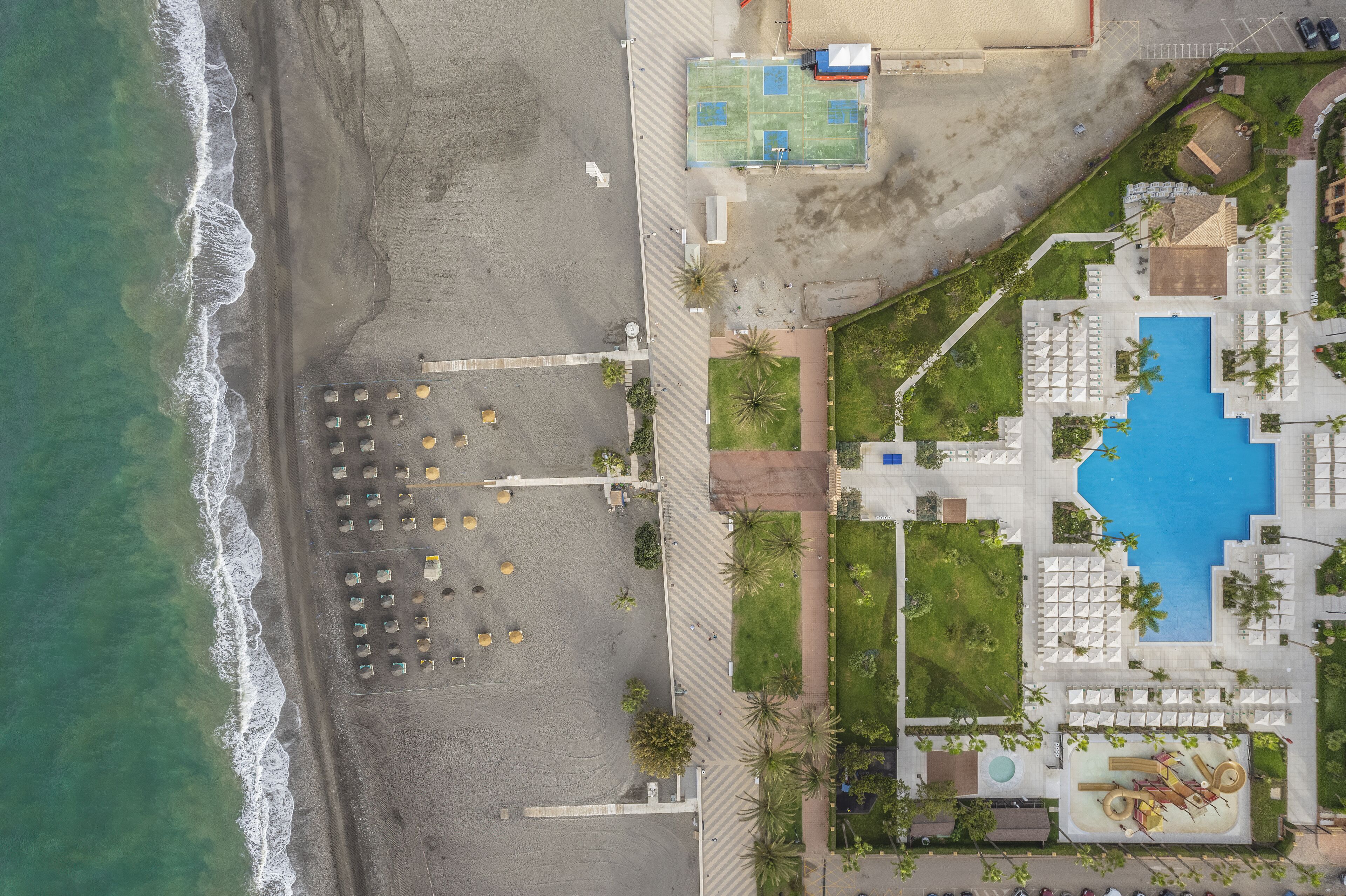 Vista aérea de un complejo turístico con playa, piscina y cancha de tenis.