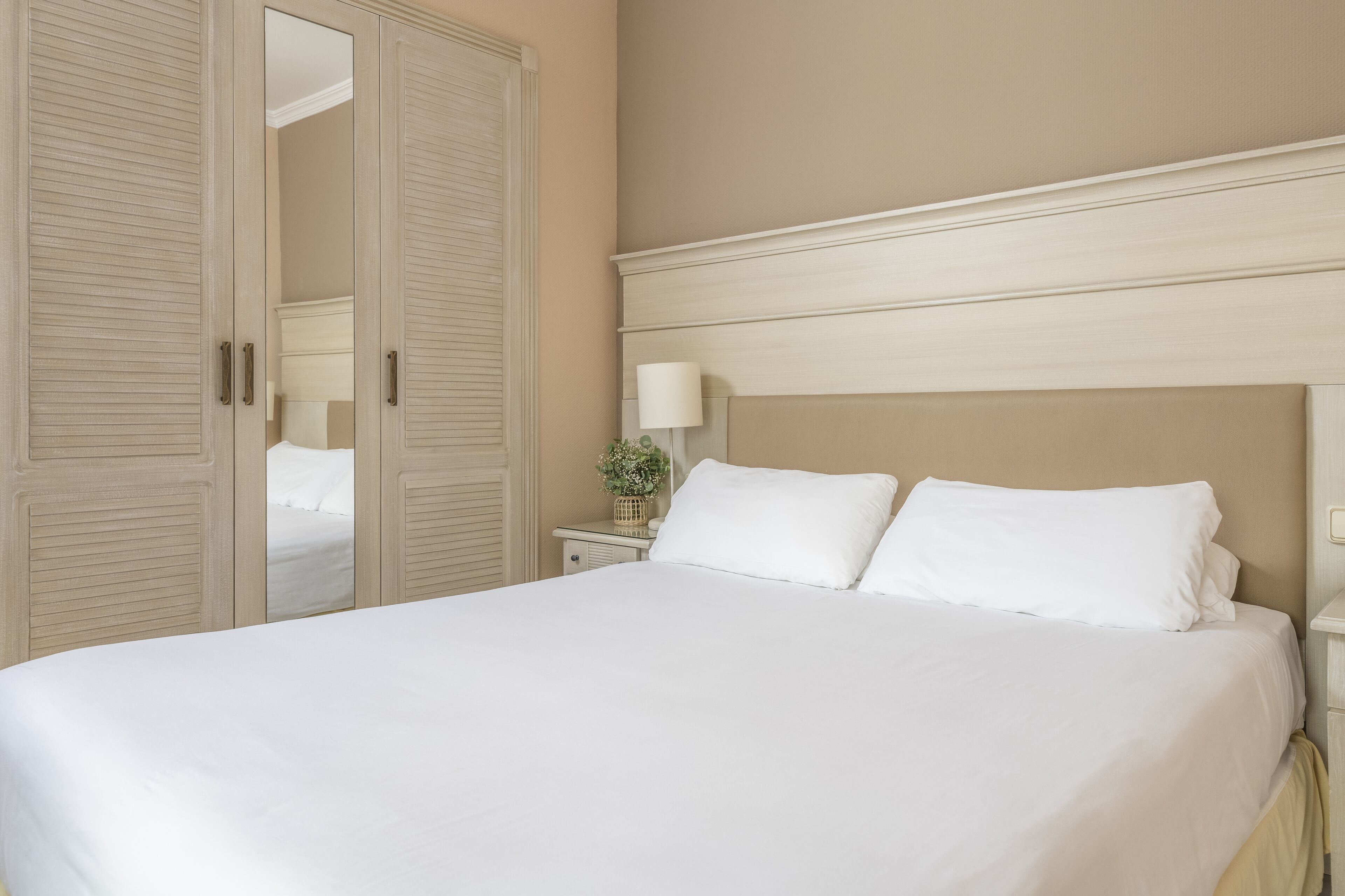 A neatly made bed with white linens, a bedside lamp, and a small plant on a nightstand.