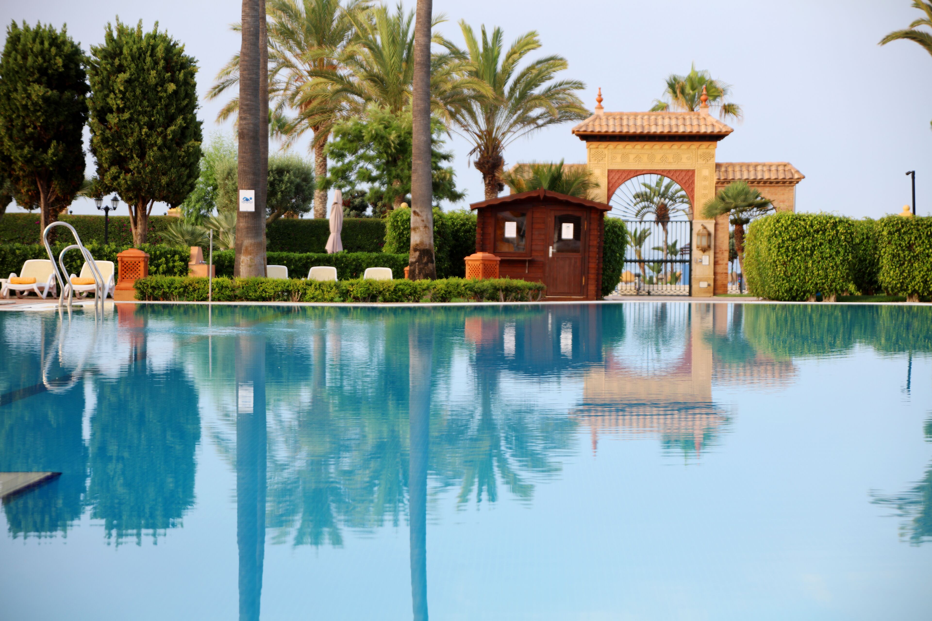A swimming pool with lounge chairs, palm trees, and a small wooden structure.