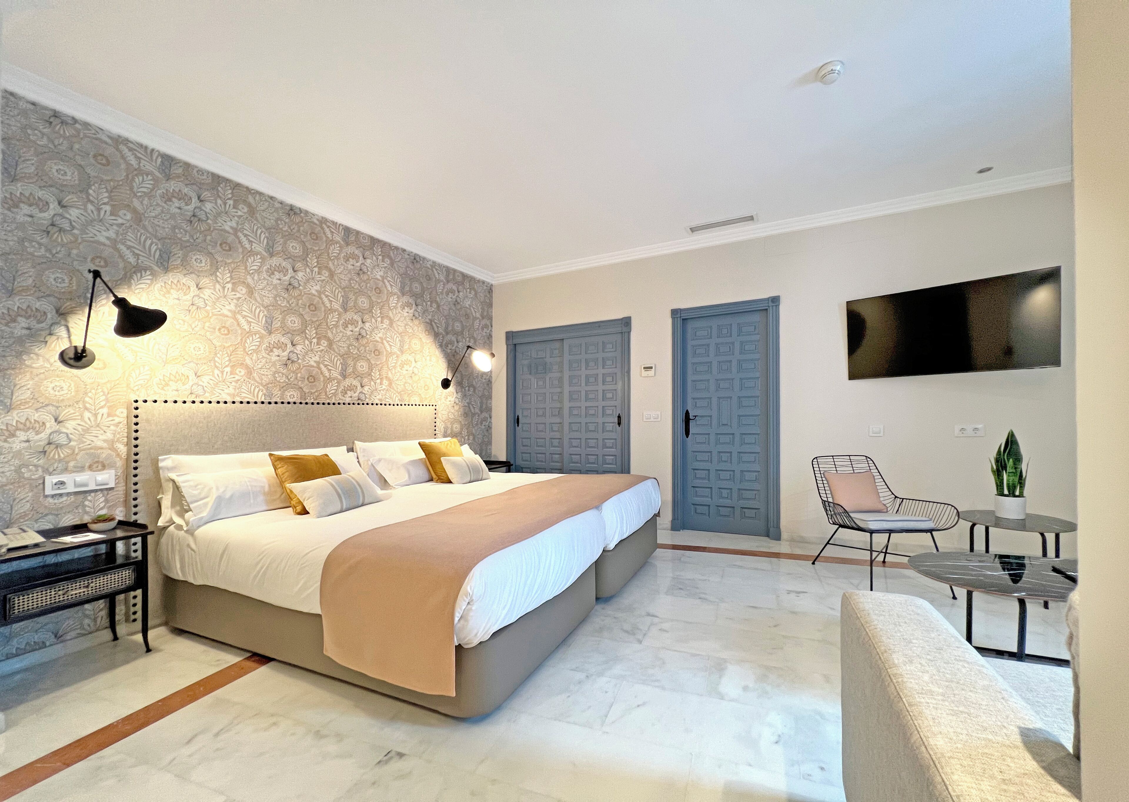 A bedroom with a bed, bedside tables, a desk, a chair, a TV, and a door.