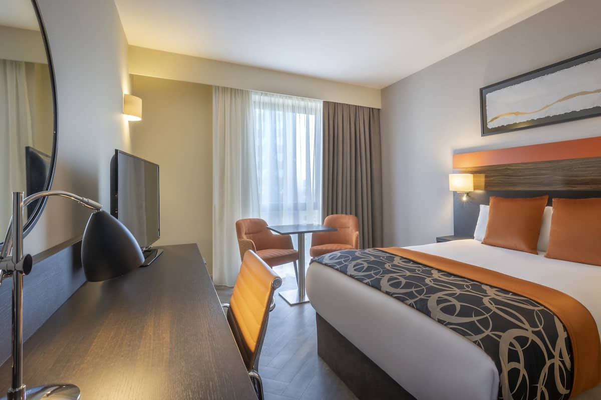 A hotel room with a bed, a desk, a chair, a TV, and a window with curtains.