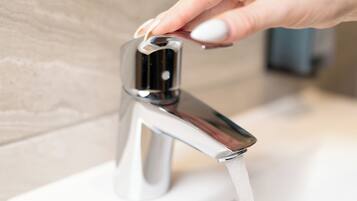 A hand turning a modern, chrome faucet with water flowing into a white bathtub.