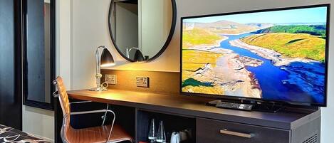Une chambre d’hôtel comprenant un lit, un bureau avec une chaise, une télévision, un miroir et une armoire.