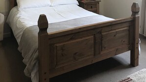 A bedroom with a wooden bed, a nightstand with a lamp, and a ceiling light. - The Anchor Inn (March)