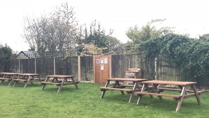 A grassy outdoor area with picnic tables and a small wooden structure. - The Anchor Inn (March)