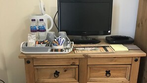 A wooden desk with a computer monitor, keyboard, and various office supplies. - The Anchor Inn (March)