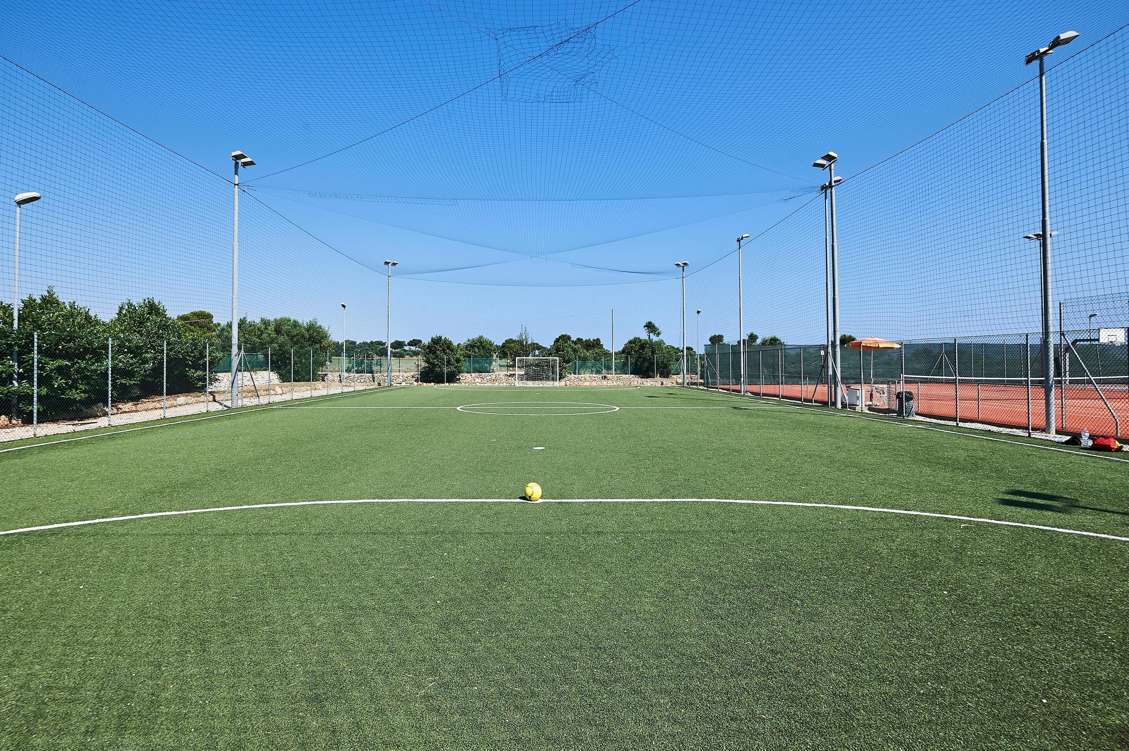 A sports field with a goalpost, surrounded by fencing and street lamps.