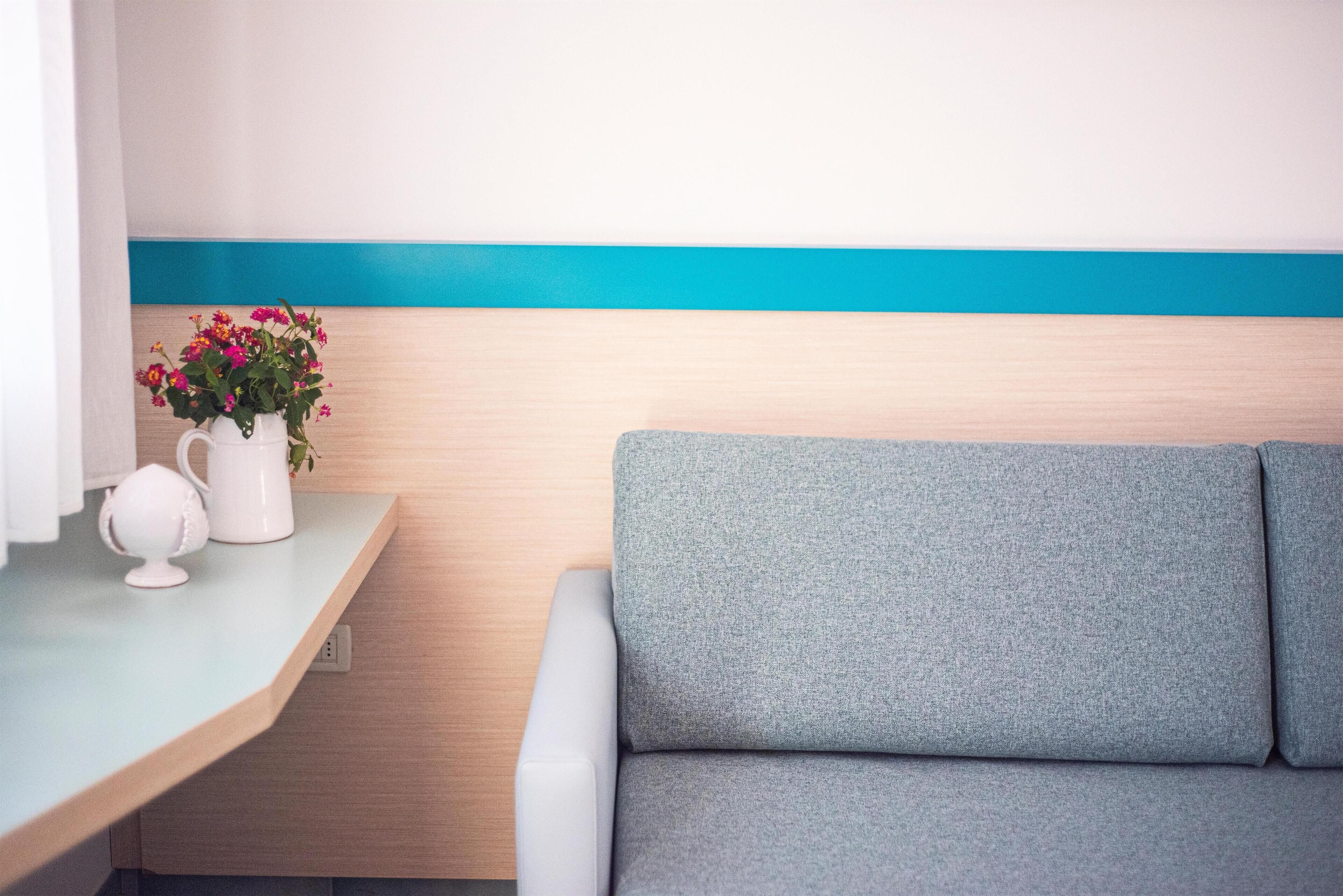Ein modernes Zimmer mit einem grauen Sofa, einer weißen Vase mit Blumen und einer hellblauen Akzentwand.