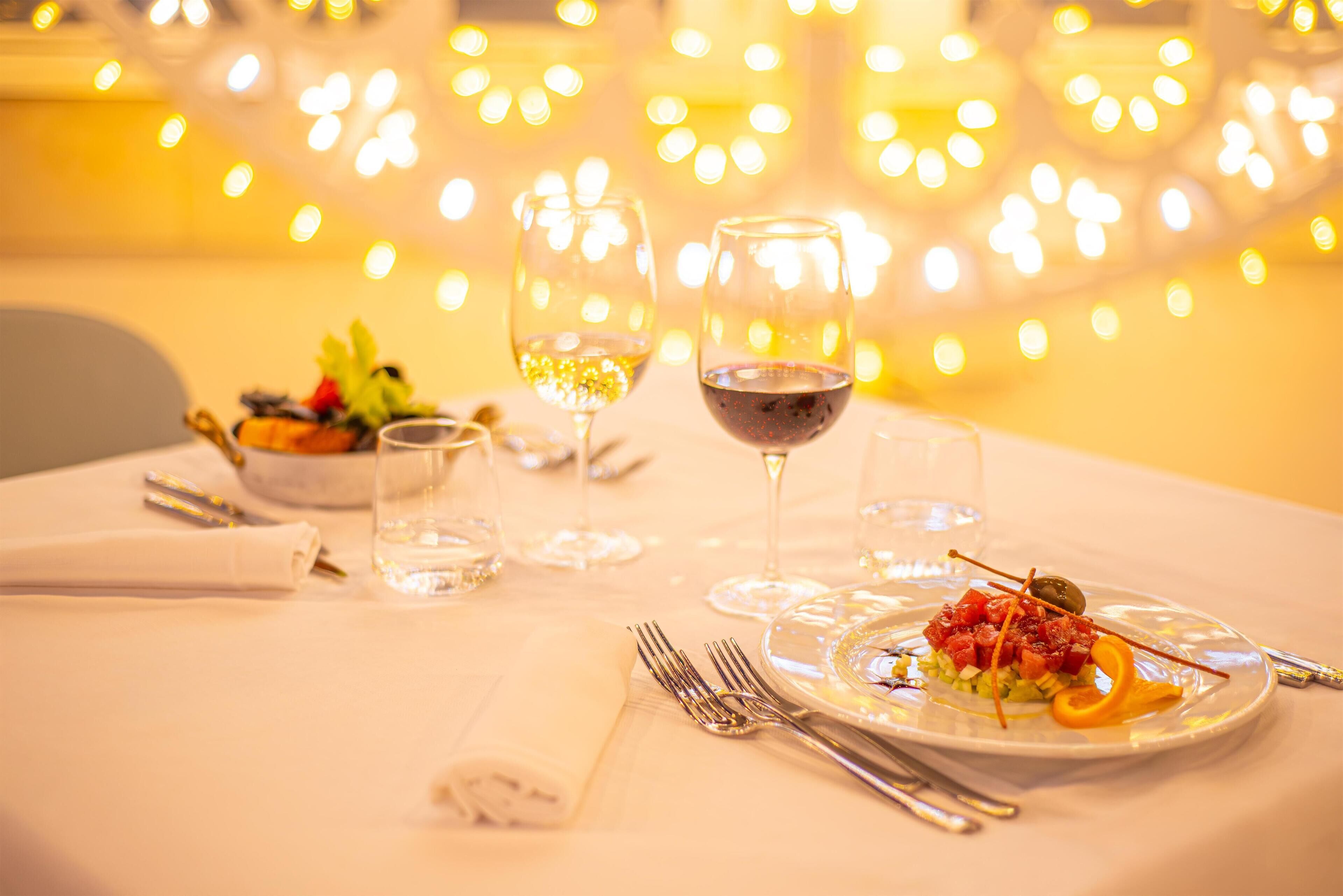 A dining table set with plates, cutlery, and glasses, with a blurred background of lights.