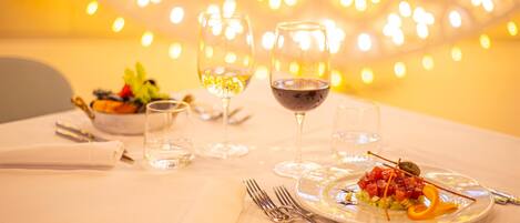A dining table set with plates, cutlery, and glasses, with a blurred background of lights.