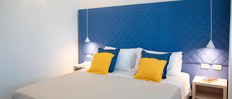 Un lit bien fait, avec une tête de lit bleue, deux tables de chevet avec des lampes et une étagère près du lit sur laquelle repose un livre.