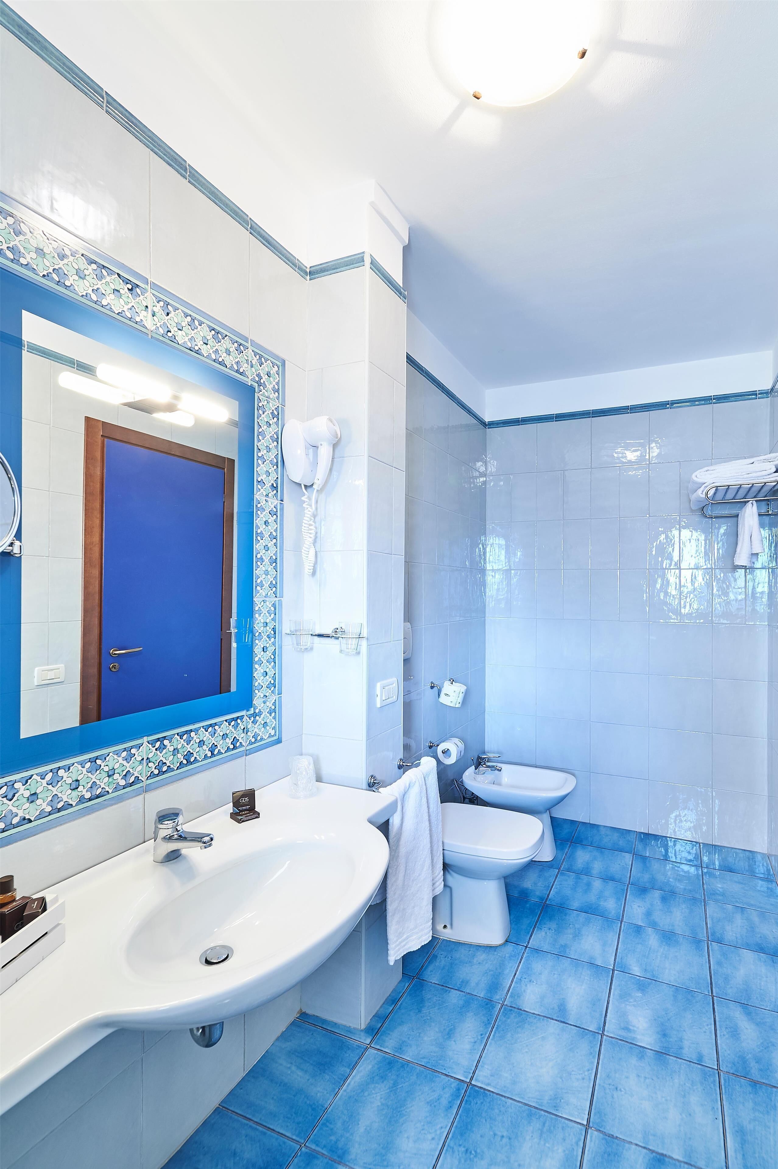 Un baño con suelo de azulejos azules, un lavabo blanco, un inodoro y un espejo con marco azul.
