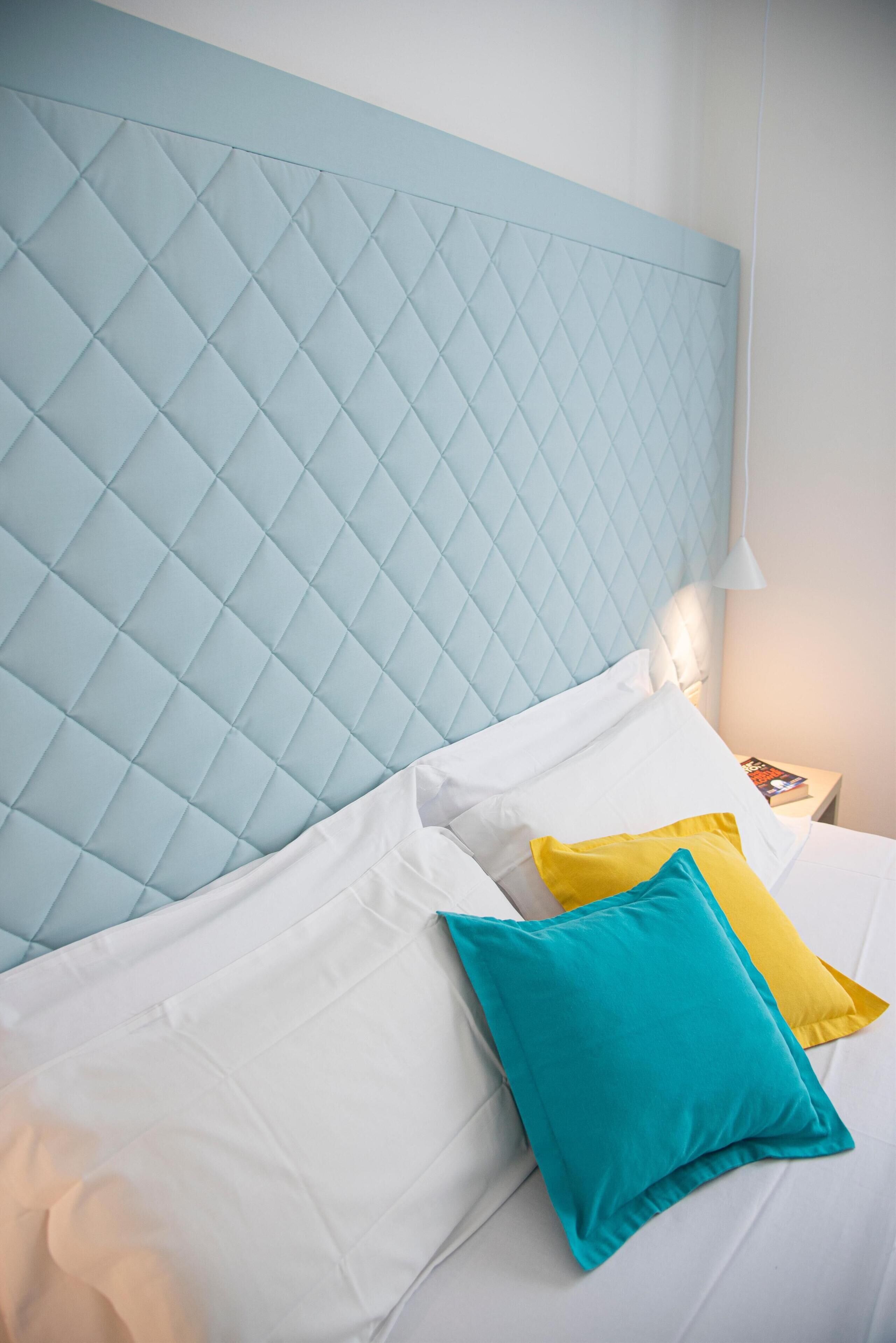 A bed with a quilted headboard, white and yellow pillows, and a teal accent pillow.