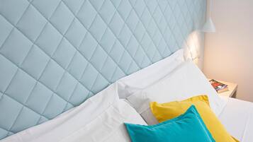 Una cama con cabecera acolchada, almohadas blancas y amarillas, y un cojín de acento color turquesa.