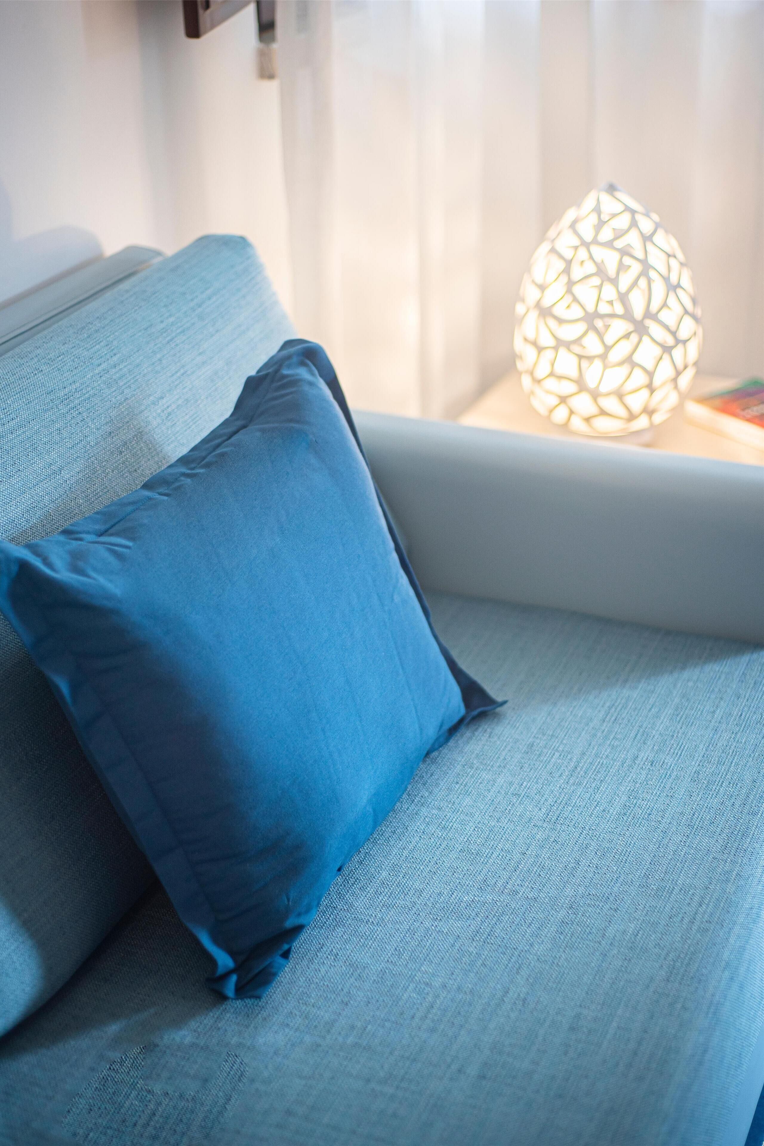 A modern sofa with a blue cushion and a geometric light fixture on a bedside table.