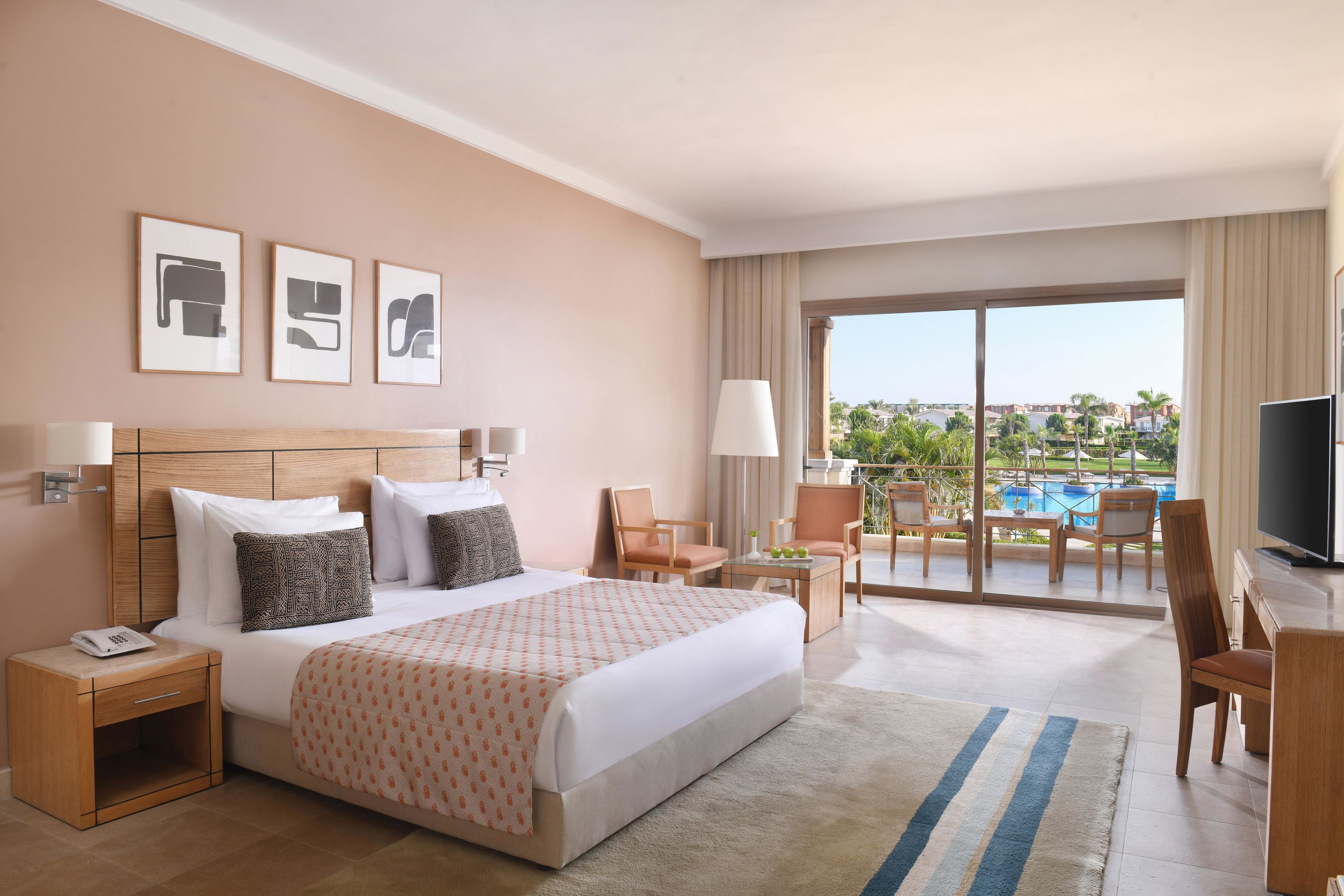 Habitación de hotel con una cama grande, un escritorio, una silla, un televisor y vista a una piscina.