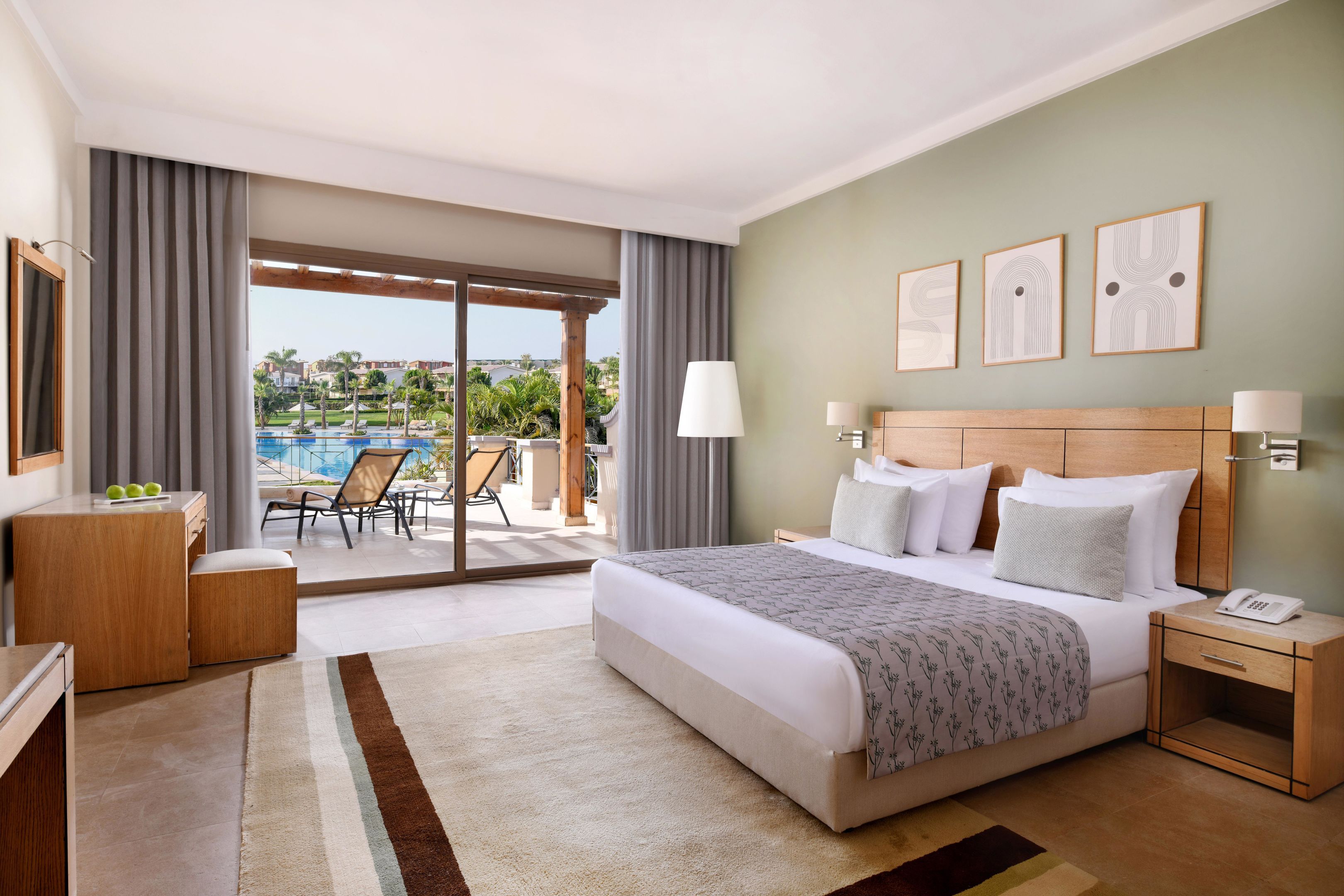 Quarto de hotel com cama, mesa de cabeceira, escrivaninha com cadeira, vista para uma piscina e varanda.