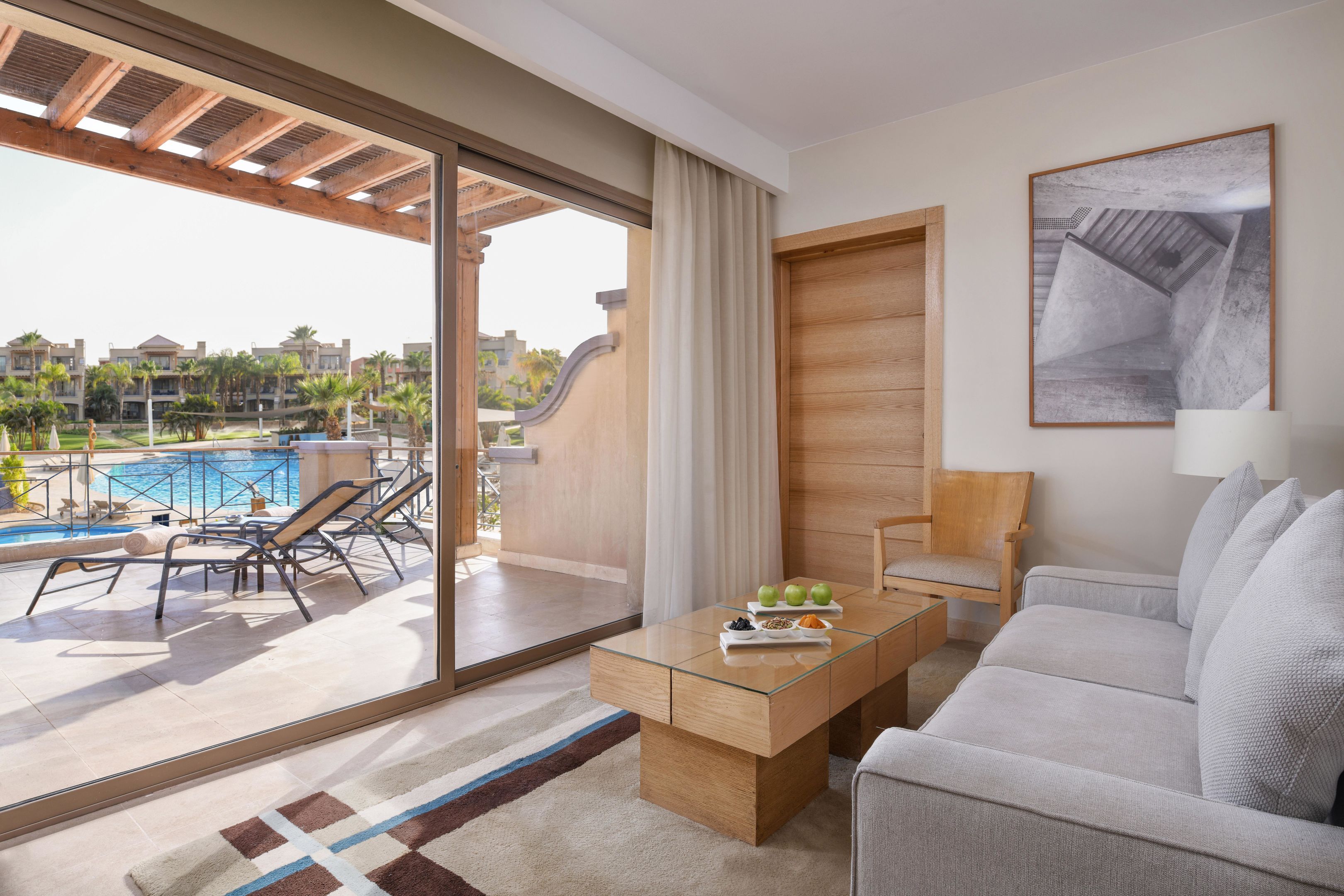 Una habitación de hotel moderna con una puerta corredera de vidrio que da a una zona de piscina, un sofá, una mesa de centro y una puerta de madera.