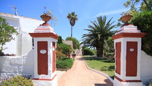 Un camino que lleva a un edificio de paredes blancas y rojas, rodeado de follaje y palmeras.