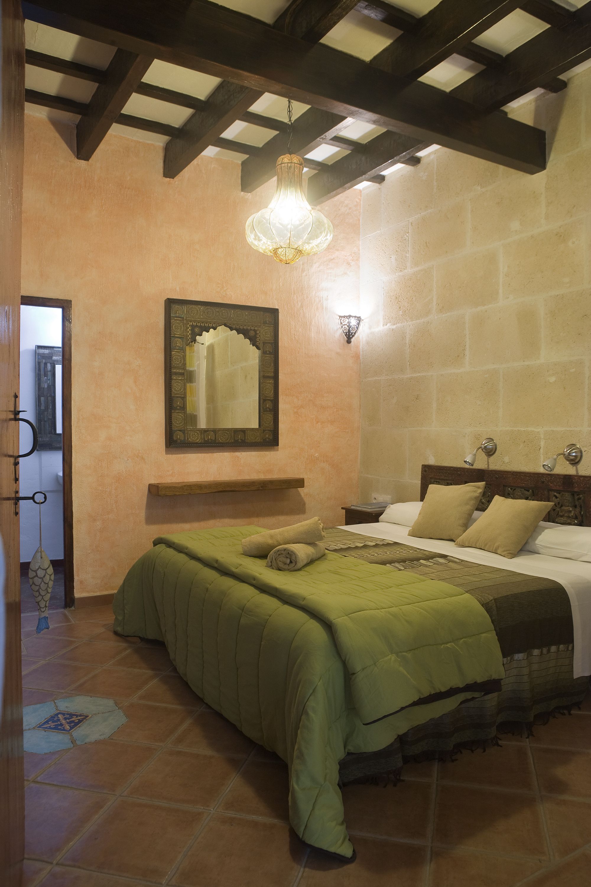 Un dormitorio con una cama, una mesita de noche, un espejo en la pared y una lámpara colgante.
