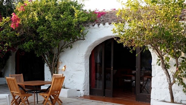 Un patio al aire libre con una mesa y sillas, rodeado de muros blancos y un piso de baldosas.