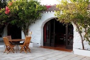 Un patio al aire libre con una mesa y sillas, rodeado de muros blancos y un piso de baldosas.