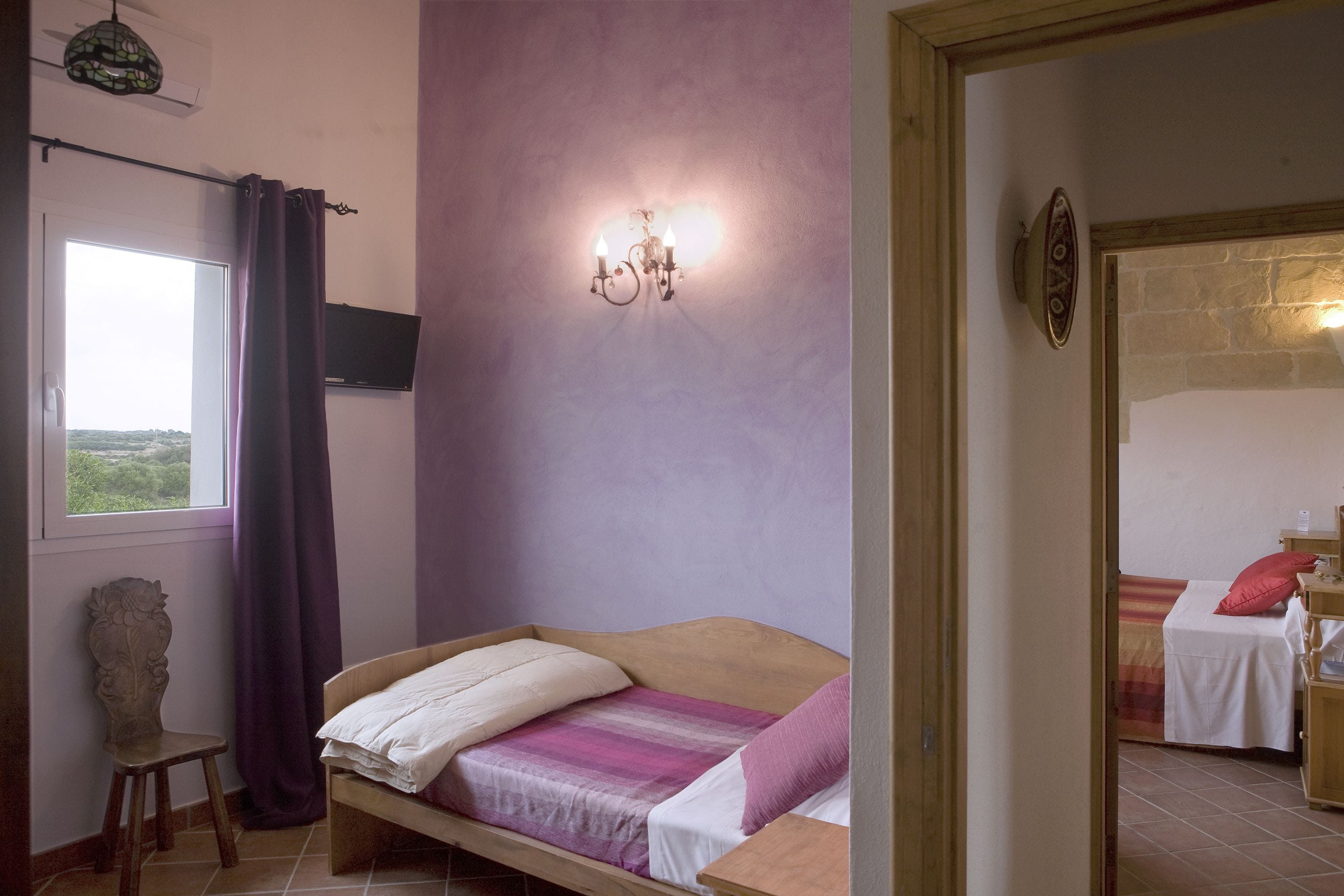 Un dormitorio con cama, una ventana con cortinas, una lámpara de pared y vistas al exterior.