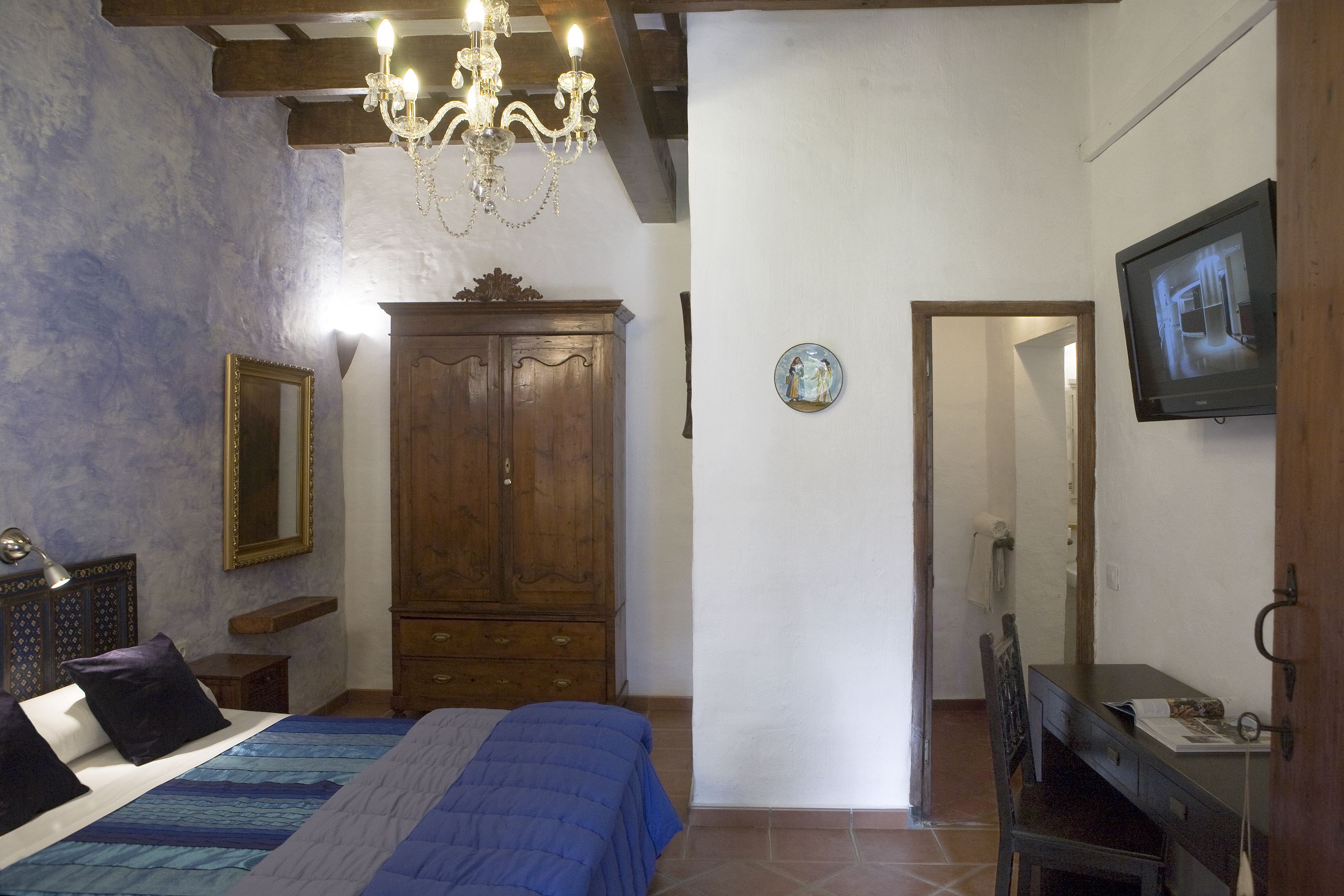 Un dormitorio con cama, armario de madera, lámpara de araña y televisor en la pared.