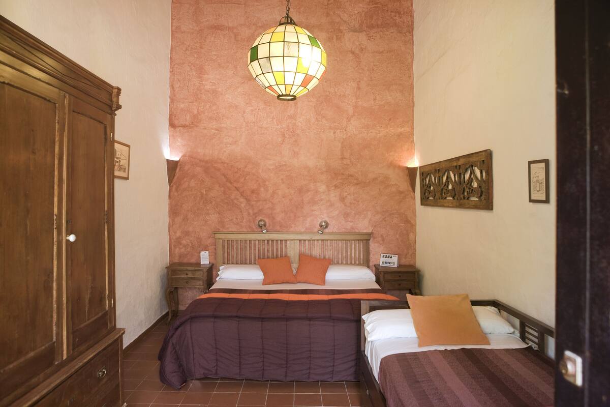 A bedroom with two beds, a wooden wardrobe, a hanging globe light, and a wall-mounted artwork.