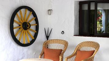 Una habitación con dos sillones de mimbre y una pequeña mesa redonda, una gran rueda decorativa en la pared y una ventana con vistas a la vegetación.