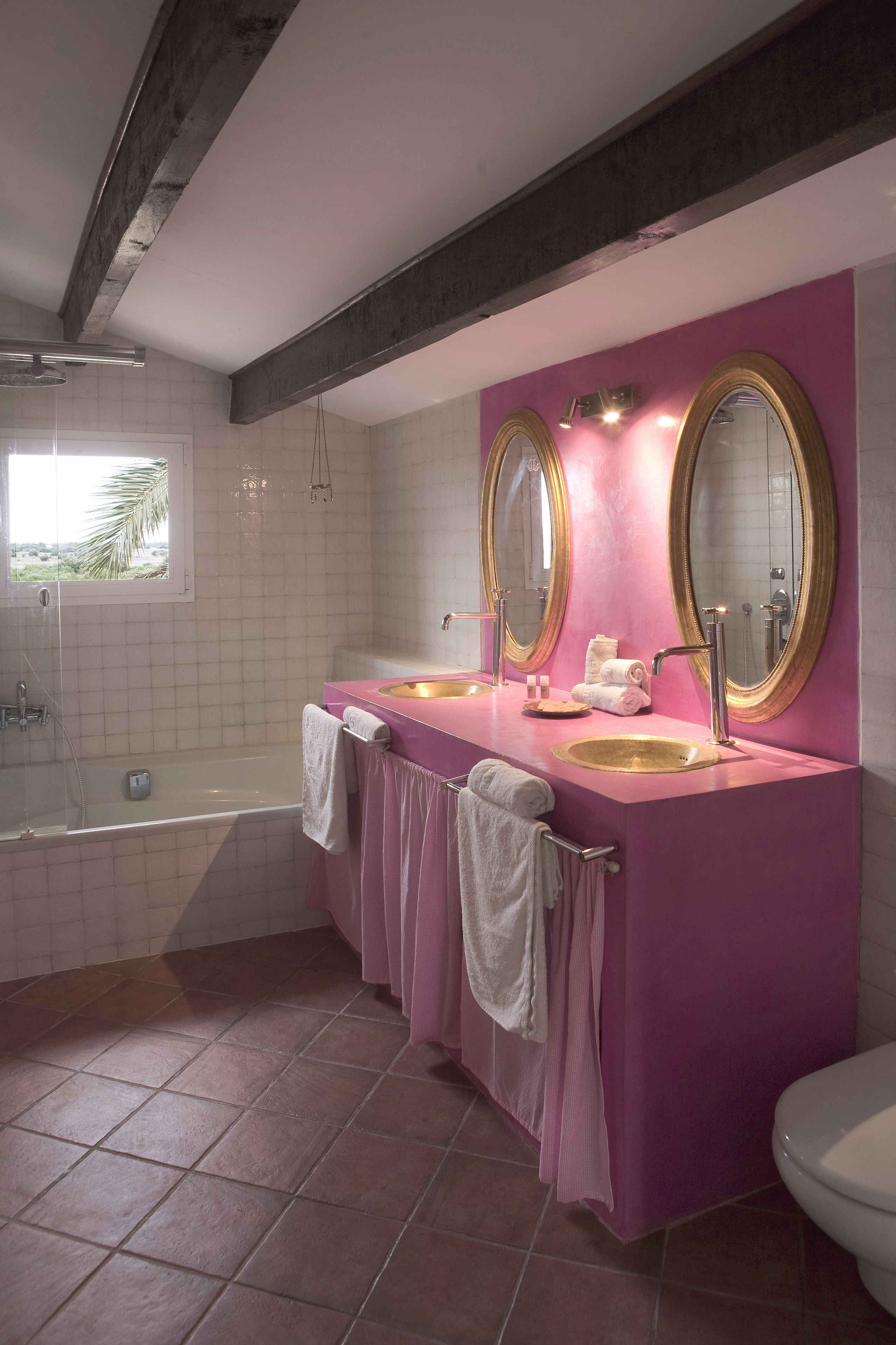 Un baño con tocador rosa, dos espejos con marcos dorados, una bañera y un inodoro.