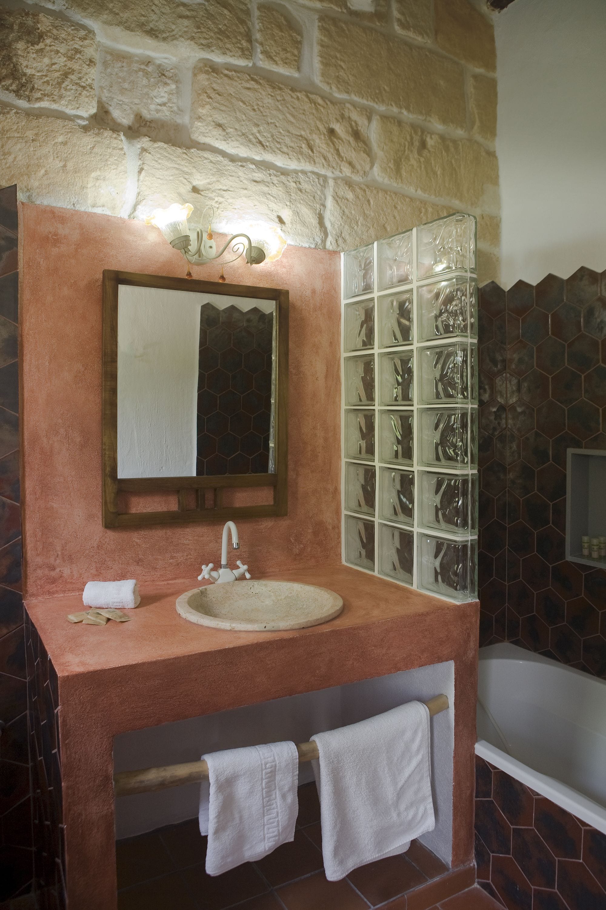 Een badkamer met een stenen muur, een houten wastafelmeubel, een wastafel, een spiegel en een glazen douchecabine.