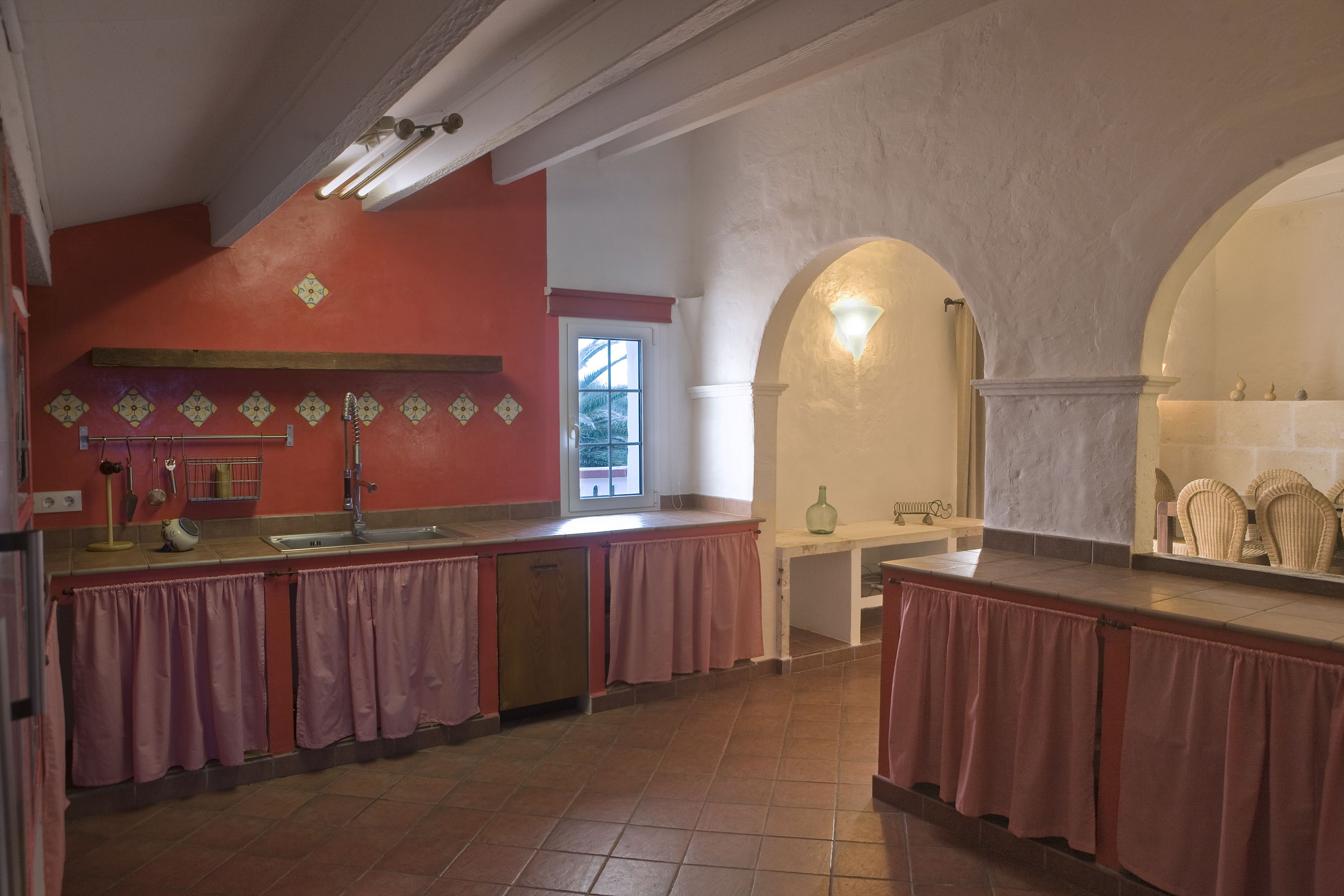 Una cocina con pared roja, un lavamanos y una ventana.