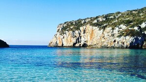 Escena costera con agua turquesa cristalina, una playa arenosa y acantilados rocosos.