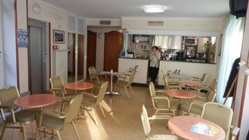 A restaurant with round tables and chairs, a kitchen area, and a person standing near the counter.