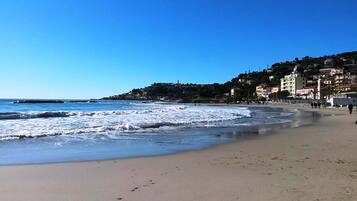 Ein Strand mit Wellen, blauem Himmel und Gebäuden im Hintergrund.