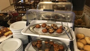 Zona de bufé con bandejas de muffins y pasteles, platos apilados al lado, y una persona al fondo.
