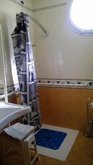 Ein Badezimmer mit Duschvorhang, der eine Collage aus Bildern zeigt, einem kleinen Fenster und einer blauen Matte auf dem Boden.