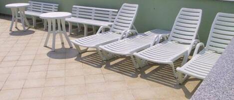 Una terraza en la azotea con sillones blancos y pequeñas mesas redondas.