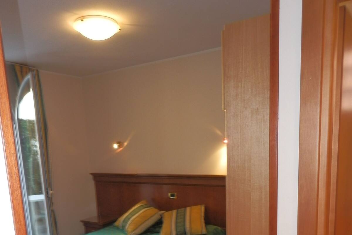 A bedroom with a bed, a wooden headboard, a nightstand, and a window with a view of trees.
